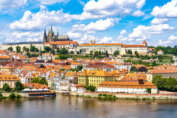 Obraz premium Prague from above the historic quarters of Mala Strana, Prague Castle, and the calm waters of the Vltava River framed by summer greenery and a blue sky.Prague,Czech Republic