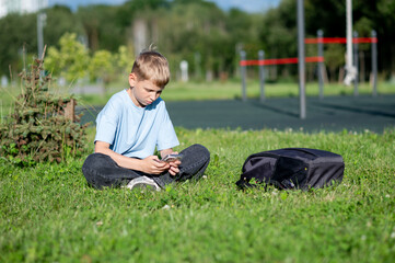 Teen boy absorbed in smartphone on green lawn, concept of gadget addiction and youth lifestyle