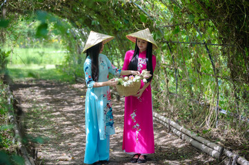 Two young female Vietnamese women in colorful Aodai national dress holding lotus flower basket in...