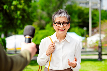 Mature businesswoman in glasses smiling during an outdoor interview in a contemporary urban park...