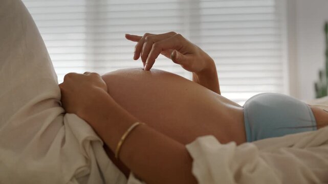 Pregnant mother plays with her fingers on tummy as baby kicks in belly