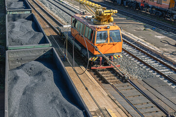 A crane on a small railway locomotive for the repair of railway tracks. Repair equipment on the railway.  Freight wagons filled with coal. Transportation of industrial raw materials by rail.