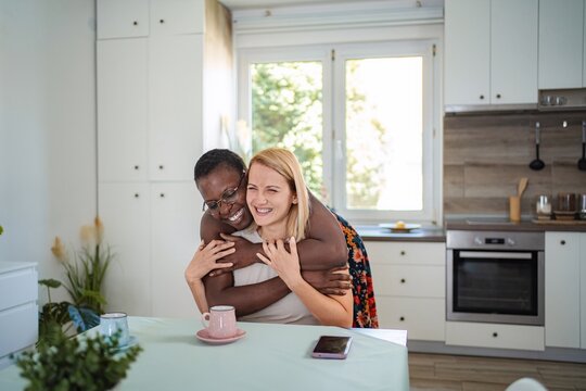 Two cheerful female friends are hugging in the kitchen