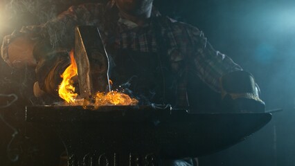 Close-up of blacksmith forging glowing hot iron on anvil with flying sparks