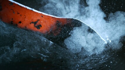 Blacksmith puts the red-hot forged metal part into cold water , close-up