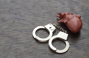 A stark conceptual image of a human heart model with miniature handcuffs, symbolizing the illegal...