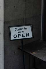 Eye-level shot of a 'Come In We're Open' sign positioned outside a building, hinting at business...