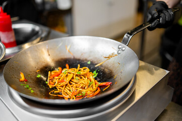 Chef stir-frying noodles with vegetables in a wok over stovetop in a professional kitchen. Asian cuisine, vibrant ingredients, dynamic cooking process