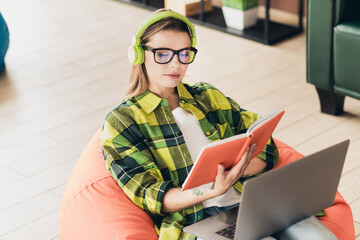 Young woman reading while listening to music with headphones at a cozy workspace, working on a...