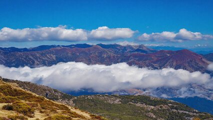 Naklejka premium Layered Mountain Landscape Under Blue Sky with White Clouds