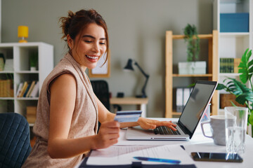 Smiling businesswoman making online payment using laptop and credit card at home office