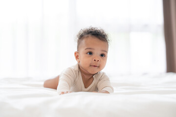 Fototapeta premium African adorable baby boy lying on bed cheerful innocent in bedroom. Happy infant with curly hair newborn cheerful crawling pose joyful indoor on bed at home