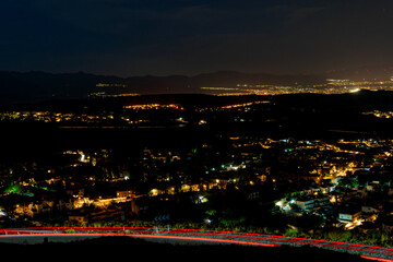 Naklejka premium Night Panorama of Granada, Andalusia, Spain, with Illuminated City Lights, Mountain Silhouettes, and Light Trails on Winding Roads