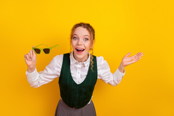 Joyful student expressing surprise and enthusiasm holding green glasses against a vivid yellow...