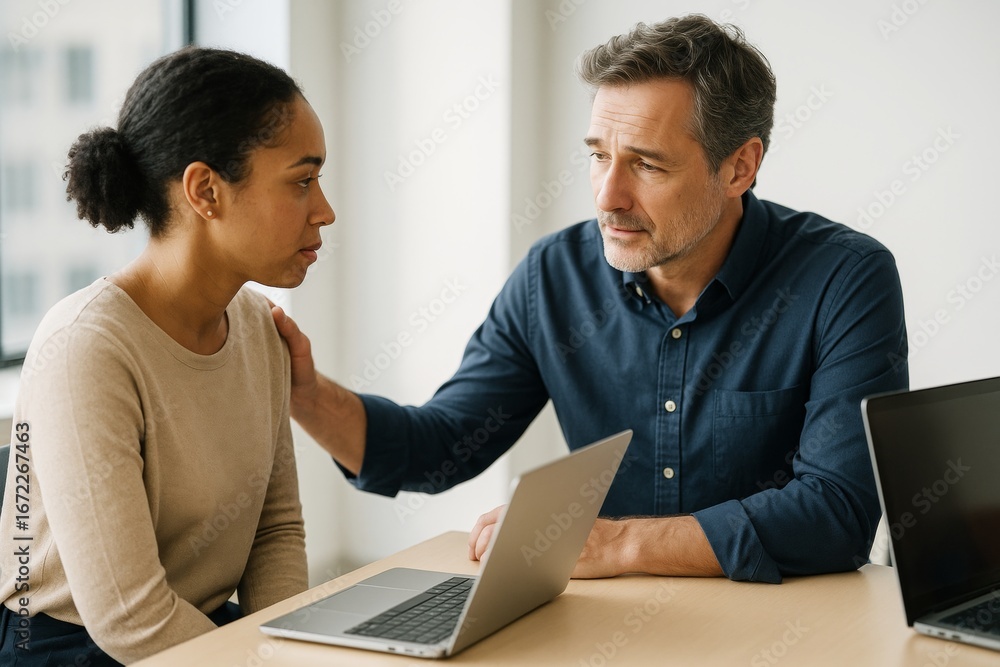 Poster empathetic coworker comforting distressed colleague during serious conversation at work with laptops