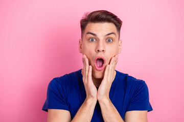 Surprised young man in blue t-shirt standing against a pink background shows astonished expression...