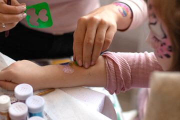 selective focus. decorative cosmetics for children and adults. holy Flash tattoo. Transfer tattoos for kids. master makes a girl a transfer temyporar glitter tattoo with sequins. childreay. Animators