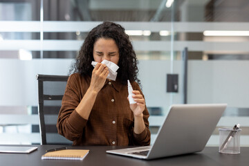 Woman sneezing in an office environment holding tissue and nasal spray