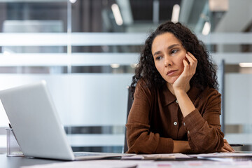 Tired professional woman looking at a laptop in a modern office.