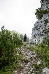 Obraz premium A view from behind of a hiker walking on a rocky mountain trail. The image captures the challenge and beauty of exploration, with the sky and peaks merging.