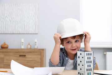 Choice of profession. Little kid in hard hat pretending to be engineer at table indoors