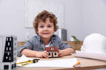 Choice of profession. Little kid in hard hat exploring house model at table indoors