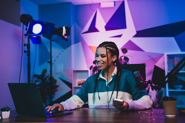 Radio host woman broadcasting a podcast in a vibrant home office, with colorful lighting and modern...