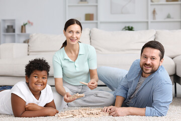 Adoption. Parents and their son playing with wooden blocks on floor at home