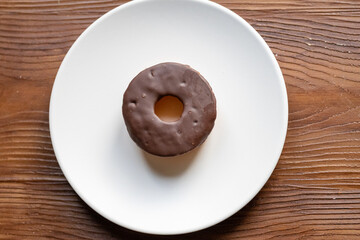 Close-Up of a Chocolate Donut on a White Plate on a Brown Table
