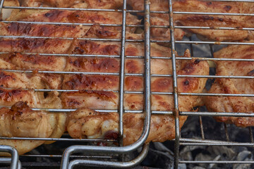 Juicy pieces of chicken are grilled in a metal grill over hot coals. The ruddy crust and smoky aroma emphasize the atmosphere of a picnic and a summer vacation in nature.