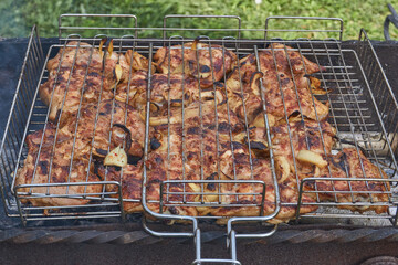 Juicy pieces of chicken are grilled in a metal grill over hot coals. The ruddy crust and smoky aroma emphasize the atmosphere of a picnic and a summer vacation in nature.