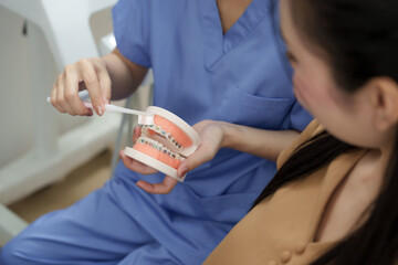 Asian female dental assistant demonstrating correct brushing technique on orthodontic model to...