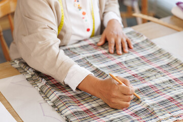 woman using a pencil to draw a pattern onto a plaid fabric on the table.
