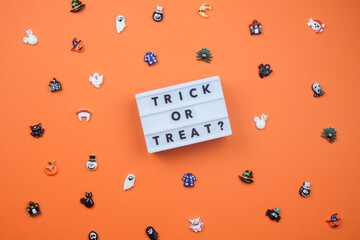 Playful Halloween flat lay: 'TRICK OR TREAT?' lightbox sign surrounded by scattered mini ghosts,...