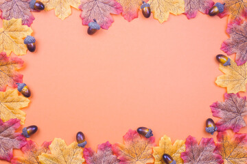 Autumn-themed background with colorful maple leaves and acorns arranged around a peach-orange space, perfect for seasonal designs, Thanksgiving, or fall promotions