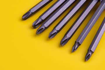 Close-up of multiple screwdriver bits arranged in a row on a bright yellow background. The metallic...