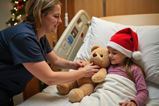 A young girl in a red Santa hat rests on a hospital bed while a nurse hands her a large teddy bear. The room is decorated with Christmas lights and ornaments