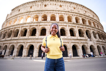 Cheerful portrait of an African American woman in Rome with the coliseum in the background, looking...