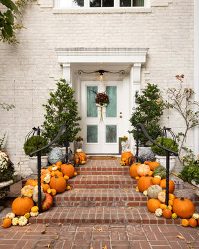 Fall, autumn in beautiful American suburban brick home with stairway entrance, leaves, and variety of pumpkins and gourds arranged artfully as decoration