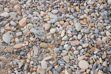 Close-up of colorful smooth pebbles covering the ground, creating a natural mosaic of shapes and...