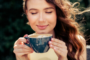Young woman enjoying a cup of coffee outdoors during a sunny day in the park, capturing leisure and...