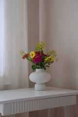 A vibrant bouquet of colorful flowers in a minimalist white vase on white table, perfect for enhancing any home decor.