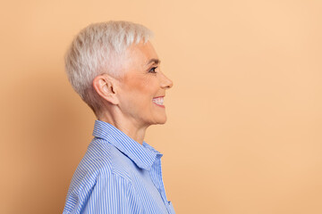 Side profile of a smiling mature woman with short white hair wearing a blue striped shirt against a beige background