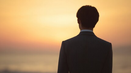 A man in a suit is standing on a beach at sunset