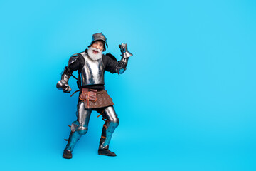Energetic senior man dressed as a medieval knight posing on a vibrant blue background