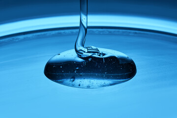 The viscous gel serum for the face flows and collects into a drop on a blue background..