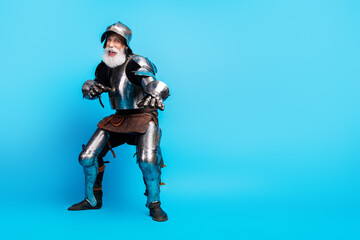 Naklejka premium Elderly man in shiny medieval knight armor posing on light blue background