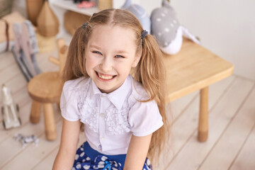 Happy caucasian young girl smiling indoors with pigtails and white blouse.