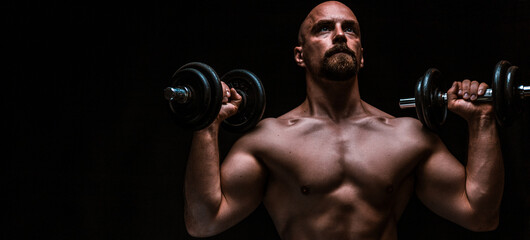 man training with a dumbbell, black background and dramatic light
