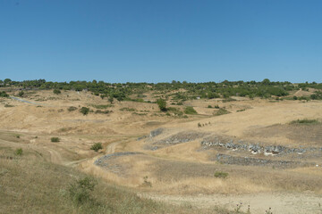characteristic terrain of Dobruja, Bulgaria, showcasing the region's unique blend of agricultural land and rolling hills. In foreground, the dry, sun-baked hills are covered in golden, parched grass.